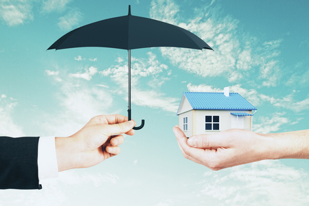 Hands holding house and umbrella on sky background. Mortgage and assuarance conceptの写真素材