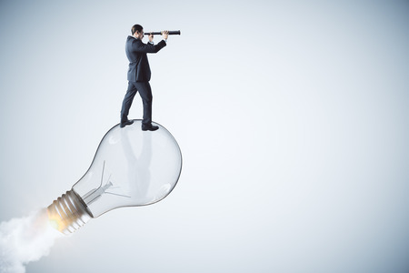 Side view of young businessman using binoculars on abstract launching lamp. Startup, idea and vision concept.の写真素材