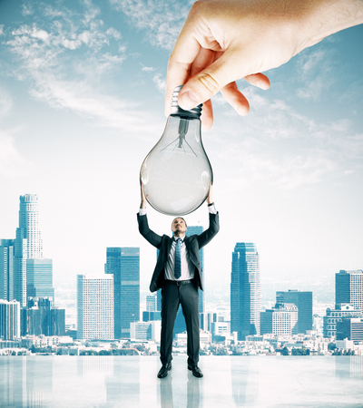 Hand handing lamp to businessman on city background. Idea and teamwork conceptの写真素材