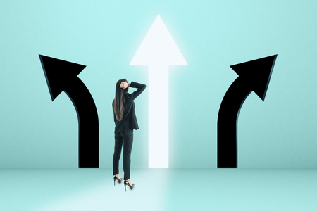 Young businesswoman with arrow choice on blue background. Different direction and way conceptの写真素材