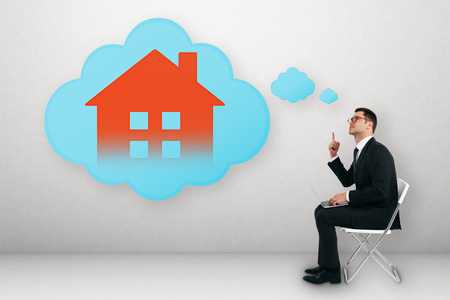 Attractive young businessman sitting on chair with laptop and thinking about digital house on concrete wall background. Smart home and app conceptの写真素材