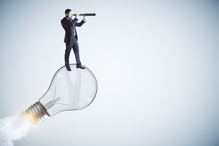Side view of young businessman using binoculars on abstract launching lamp. Start up, idea and vision concept.の写真素材