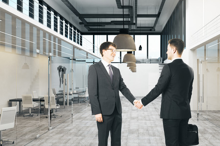 Caucasian  businessmen shaking hands in modern office interior. Teamwork and success concept.の写真素材