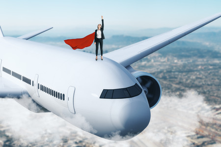 Superhero businesswoman with airplane on sky background. Confidence and leadership concept.の写真素材