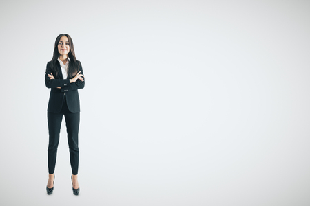 Pretty young businesswoman with folded arms standing on white background with copy space. Confidence conceptの写真素材