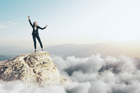 Happy businesswoman on cliff with clouds and copy space. Success and victory conceptの写真素材