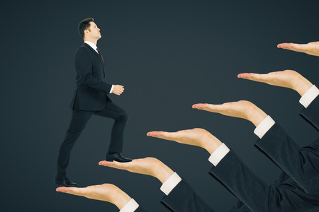 Businessman climbing hand ladder on black background. Career development and promotion conceptの写真素材