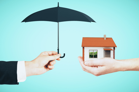 Hands holding house and umbrella on sky background. Real estate and assuarance conceptの写真素材