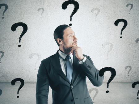 Portrait of thoughtful young european businessman with question marks. Confusion and doubt conceptの写真素材