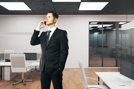 Handsome businessman talking on the phone in modern office interior. Communication, network and executives.の写真素材