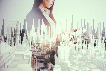Side view of beautiful young european businesswoman using tablet on abstract city background with forex chart. Technology and investment concept. Double exposureの写真素材