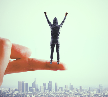 Finger holding cheerful hacker on blurry city background. Success and thief conceptの写真素材
