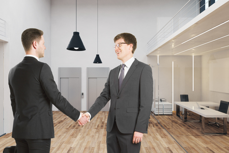 Cheerful  businessmen shaking hands in modern office interior. Teamwork and success concept.の写真素材