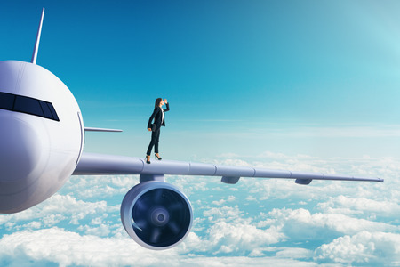 Side view of young european businesswoman looking into the distance while standing on white airplane in blue sky. Research and travel concept.の写真素材