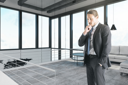 Thoughtful white businessman standing in modern office interior.の写真素材
