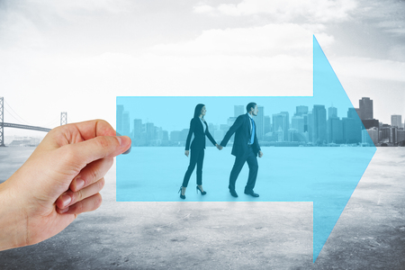 Hand holding arrow with walking businessman and woman couple on city background. Growth and partnership conceptの写真素材
