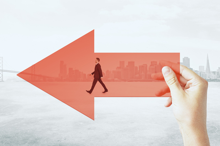 Hand holding red arrow with walking businessman on city background. Growth and startup conceptの写真素材