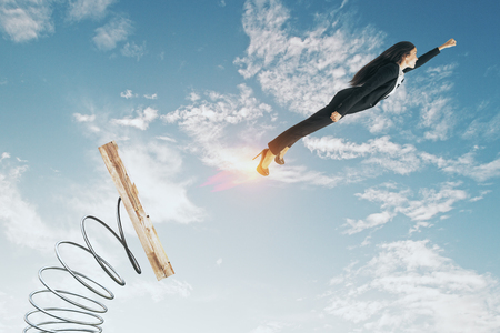 Businesswoman lauching off big spring on sky background with clouds. Startup and success conceptの写真素材
