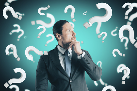 Portrait of attractive young european businessman with question marks. Doubt and confusion conceptの写真素材