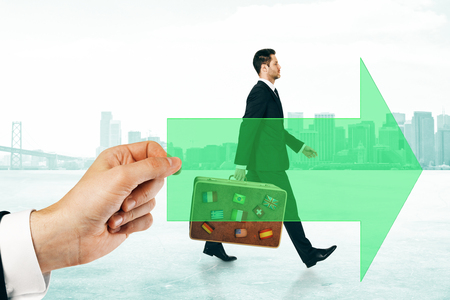 Hand holding arrow with walking businessman with travel baggage on city background. Growth and business trip conceptの写真素材