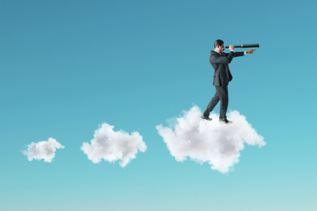 Young businessman using telescope while standing on cloud on sky background. Vision and future conceptの写真素材