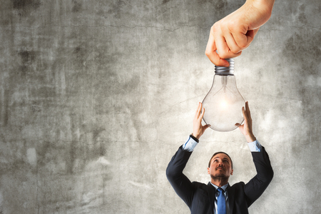 Attractive young european businessman holding lamp on concrete background. Idea and invention conceptの写真素材