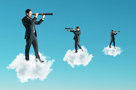 Young businessman using telescope while standing on cloud on sky background. Vision and research conceptの写真素材