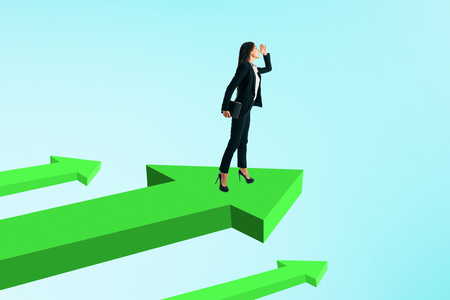 Young businesswoman looking into the distance while standing on green arrows. Sky background. Research and growth conceptの写真素材