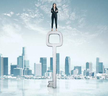 Young businesswoman standing on abstract key on city background. Access and confidence conceptの写真素材