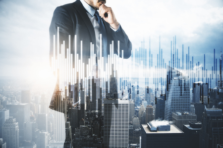 Attractive young european businessman thinking on city background with forex chart. Trade and money concept. Double exposureの写真素材