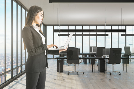 Young businesswoman using laptop in modern office with panpramic city view. Technology and communication concept.の写真素材