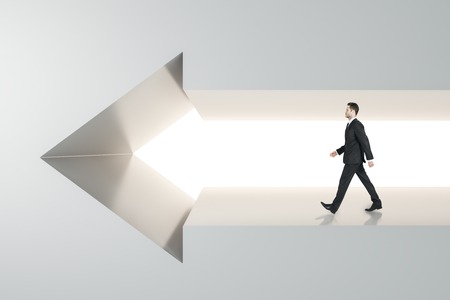 Side view of young businessman walking in arrow wall. Success and career concept.の写真素材