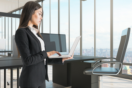 Pretty businesswoman using laptop in modern office with panpramic city view. Technology and communication concept.の写真素材