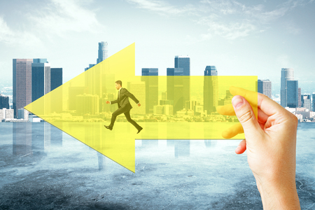 Hand holding yellow arrow with running businessman on city background. Growth and forward conceptの写真素材