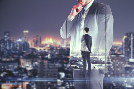 Young businessman thinking on abstract blurry night city background. Think and finance concept. Double exposureの写真素材