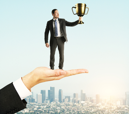 Hand holding businessman with golden cup on sky background. Leadership and success conceptの写真素材