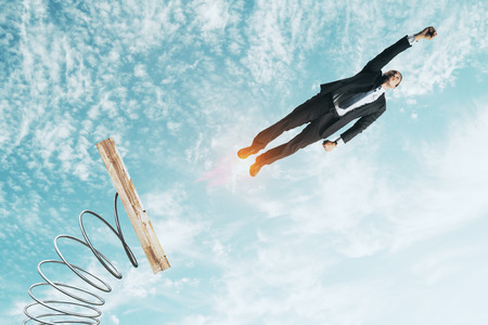 Businessman lauching off big spring on sky background with clouds. Startup and success conceptの写真素材