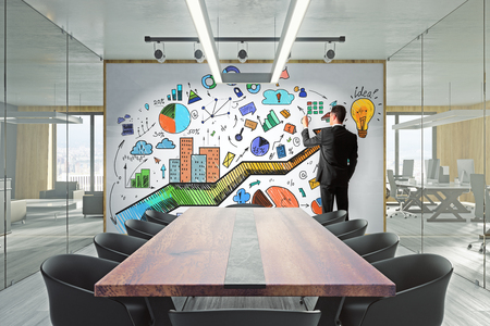 Businessman in modern meeting room with creative business sketch on whiteboard. Marketing and presentation concept.の写真素材