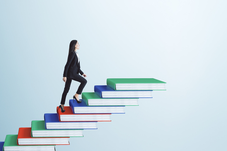 Businesswoman climbing book pile ladder. Sky background. Education and career conceptの写真素材