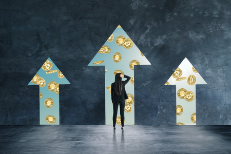 Businesswoman looking at bitcoins through arrow opening in wall. Cryptocurrency and growth conceptの写真素材
