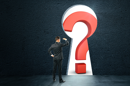 Businessman looking at question mark through key hole in wall. Doubt and access conceptの写真素材