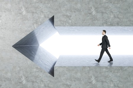 Side view of young businessman walking in arrow wall. Success and growth concept.の写真素材