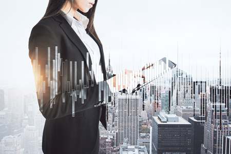 Attractive young businesswoman using tablet on abstract city background with forex chart. Trade and innovation concept. Double exposureの写真素材