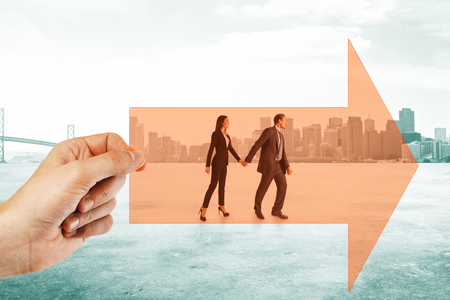 Hand holding arrow with walking businessman and woman couple on city background. Growth and teamwork conceptの写真素材