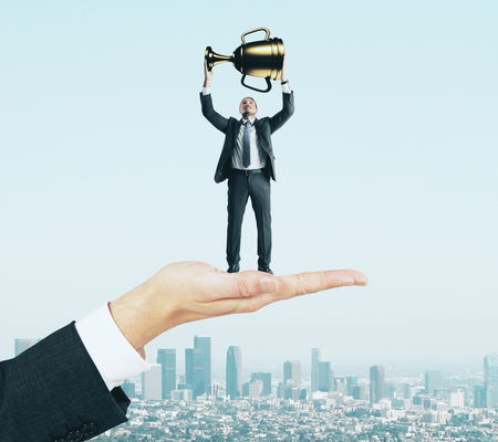 Hand holding businessman with golden cup on sky background. Leadership and growth conceptの写真素材