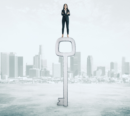 Young businesswoman standing on abstract key on city background. Access and success conceptの写真素材