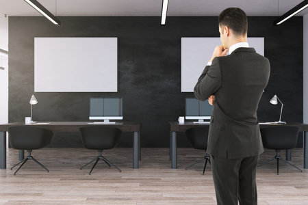 Young businessman standing in modern office interior with empty posters. Mock up,の写真素材