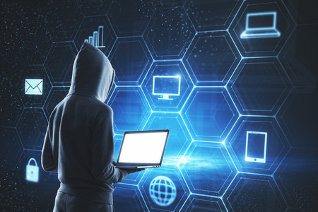 Hacker using laptop with digital business interface on glowing blue background. Hacking and computing concept.の写真素材