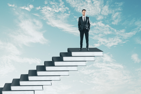 Businessman on top of book pile ladder. Sky background. Education and growth conceptの写真素材