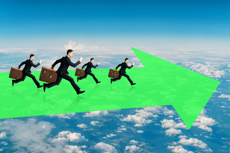 Businessmen with briefcases running on abstract green arrow. Cloudy sky background. Growth and freedom conceptの写真素材